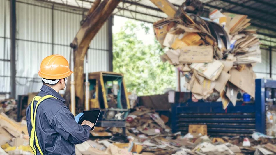 A transfer station worker watches as machinery lifts material