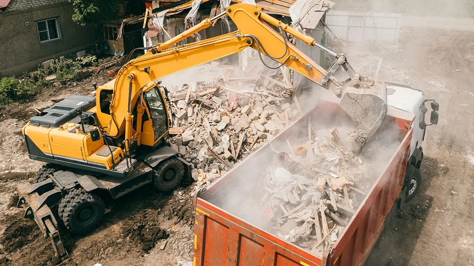 Excavator breaks building and loads construction waste into truck with its bucket
