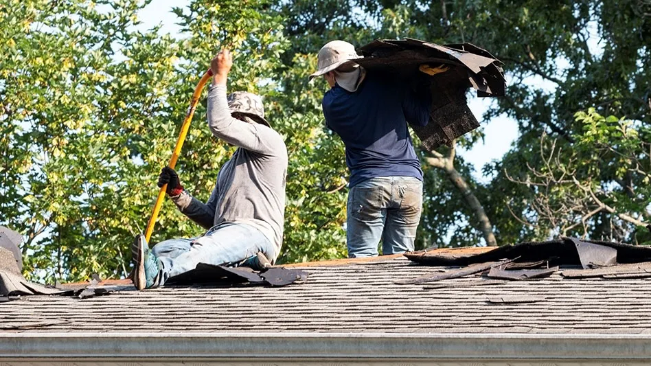 two construction workers remove shingles from roof