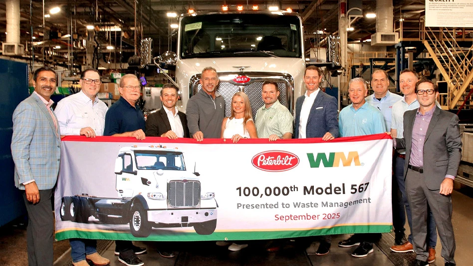 people smiling in front of refuse and construction vehicle holding banner